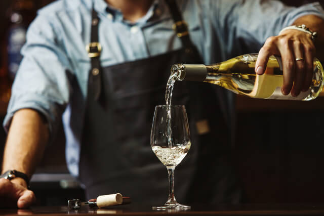 Male pouring white wine into long-stemmed wine glass